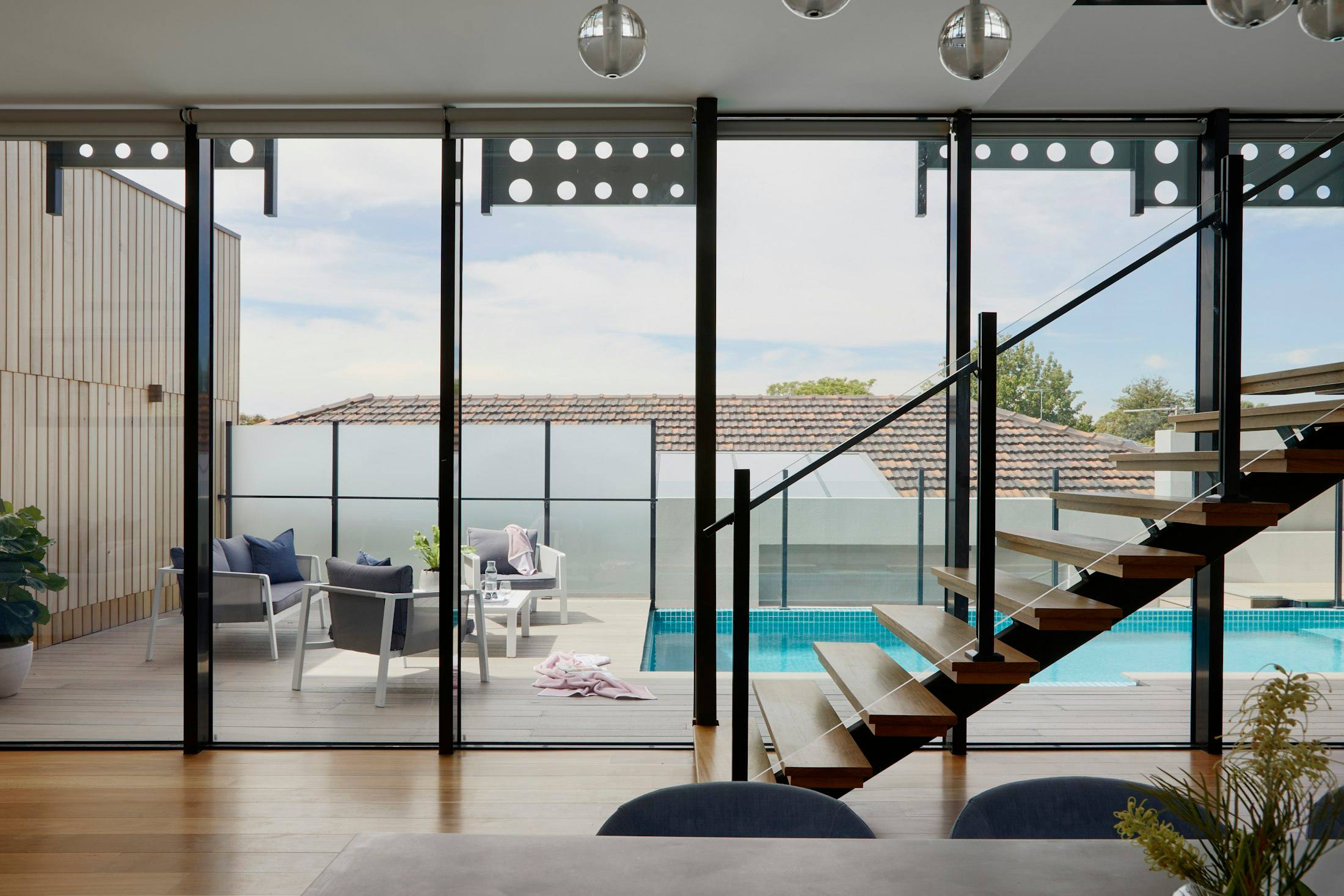 Floating wood staircase beside floor-to-ceiling glass looking out to a pool deck